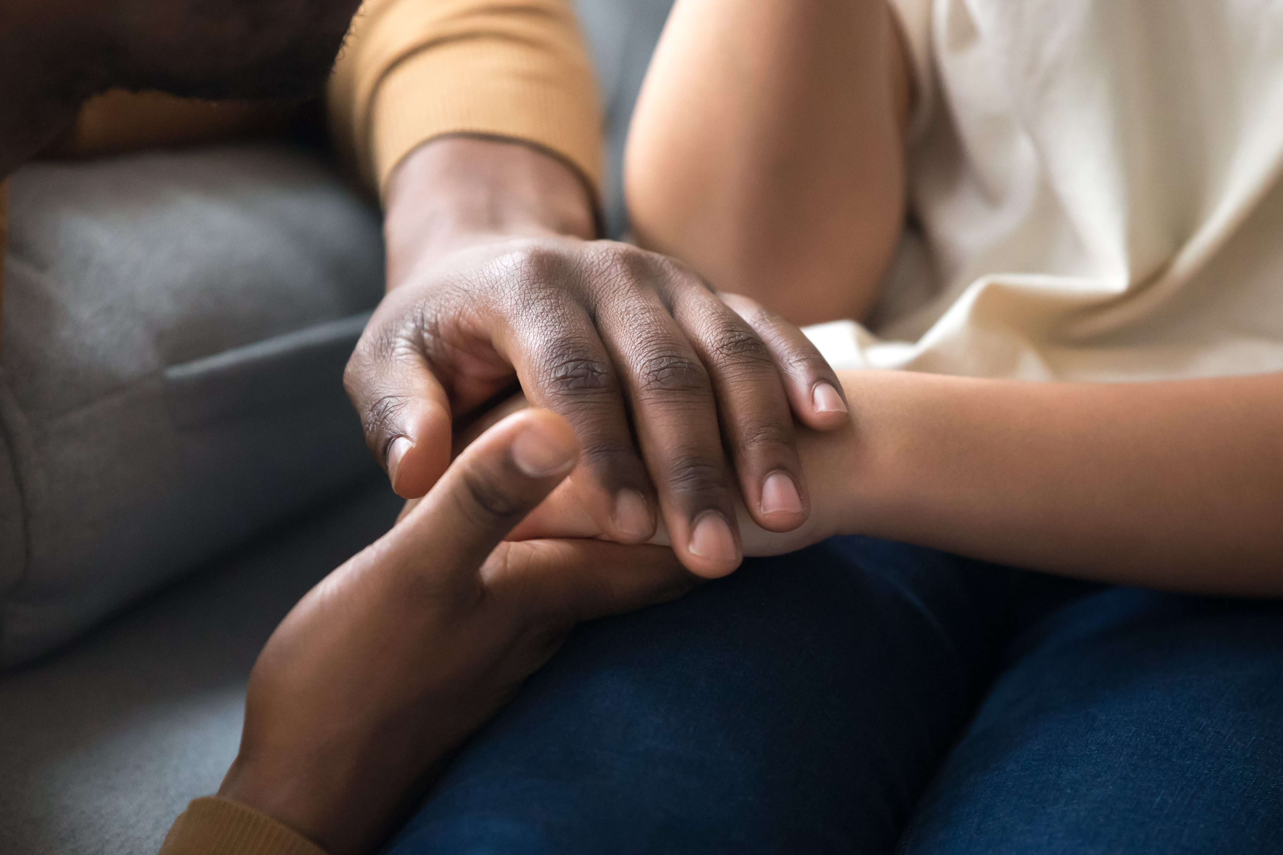 Adult hand rests on the hand of a child to comfort